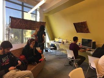 A photo of a video game being shown at an awards show exhibition. People are sitting and playing the game on computers. In the background is a banner with the game's title, I WAS HERE.