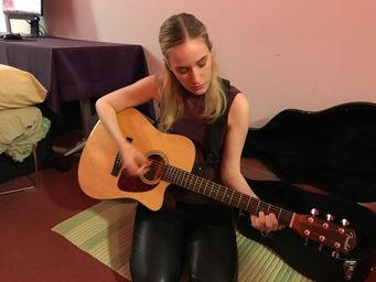 A photo of me, Chiara Gatti, playing guitar as part of the showcase exhibition for my game I WAS HERE at the 2018 NYU Game Center Student Showcase.