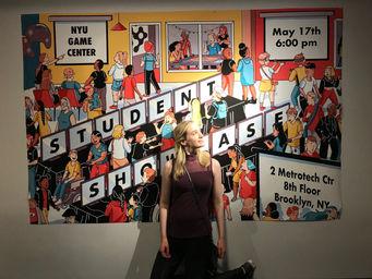A photo of me, Chiara Gatti, standing in front of a large poster for the NYU Game Center 2018 Student Showcase.